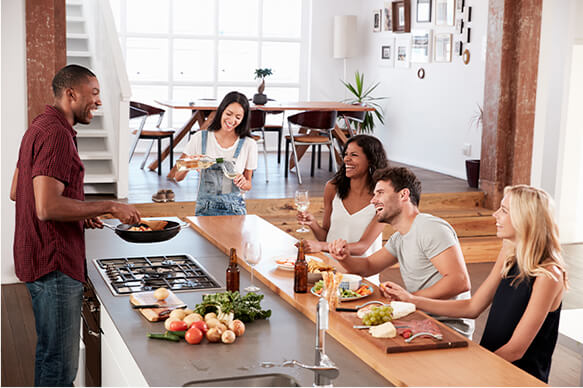 Open plan kitchen setting with five friends are enjoying a meal together with some drinks around a kitchen counter